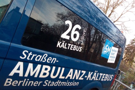Seitenansicht eines blauen Vans mit dem Aufdruck ‚26 Jahre Kältebus‘ und dem Logo der Berliner Stadtmission. Darunter steht ‚Straßen-AMBULANZ-KÄLTEBUS‘ in weißer Schrift.
