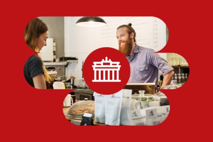 Leitbild-Wert Leidenschaft: zwei Personen im Gespräch in einem Café, überlagert von einem roten Kreis mit Brandenburger-Tor-Symbil als Hinweis auf Berlin.