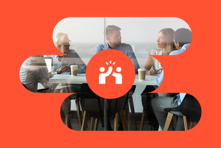 Mehrere Personen sitzen gemeinsam an einem Tisch im Gespräch; darüber ein roter Kresi mit dem Sysmbol für Zusammenarbeit und den Leitbild-Wert Miteinander.