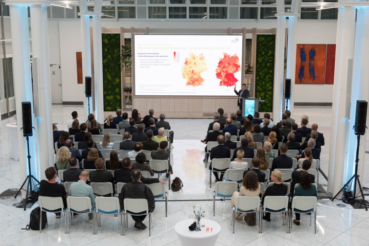 Besucher:innen des Immobiliendialoges. Im Hintergrund sieht man einen Vortragenden und eine PowerPoint-Präsentation.
