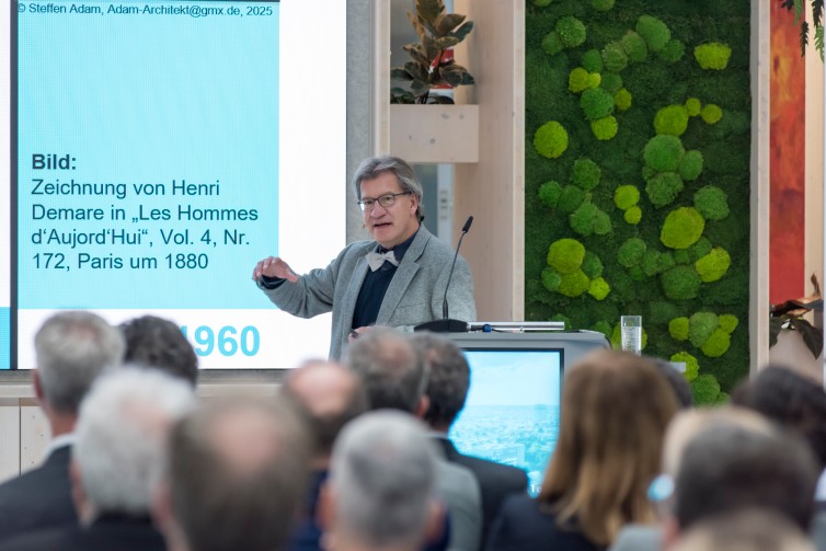 Vortragender beim Immobiliendialog 2025 mit PowerPoint-Präsentation im Hintergrund.