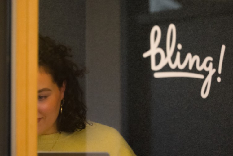 Junge Frau mit lockigem Haar arbeitet konzentriert, im Hintergrund das Bling-Logo an der Wand