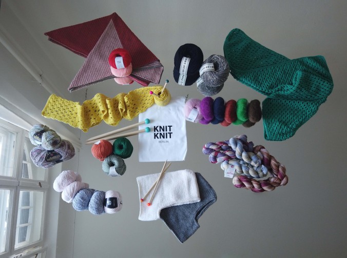 Ein Strickset mit bunten Wollknäul, Stricknadeln und Wollmützen liegt drapiert auf einem Tisch.