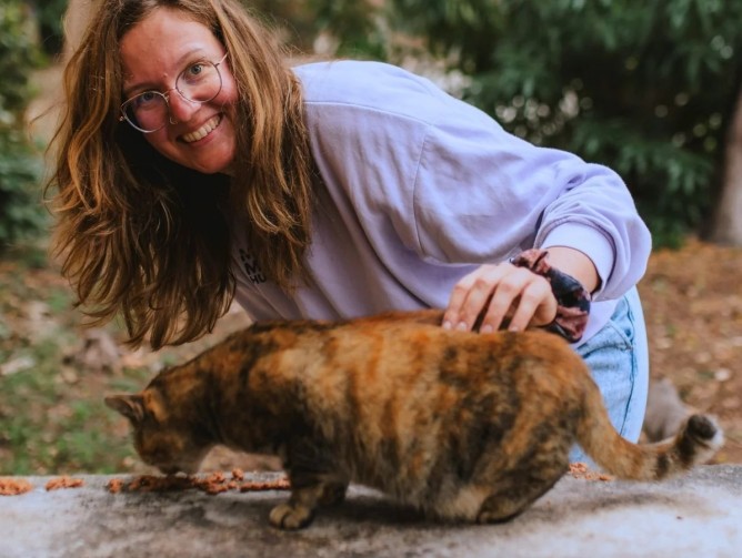 Gründerin Madeline streichelt eine Katze und schaut lächelnd in die Kamera